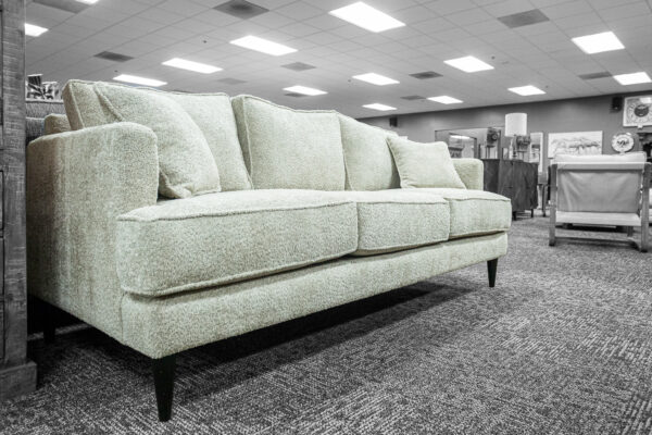 Light grey upholstered sofa with a clean silhouette and plush cushions, set against a neutral showroom backdrop.