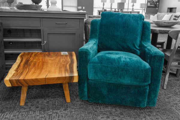 Teal upholstered armchair next to a rectangular live edge wooden coffee table, set against a backdrop of dark cabinetry.