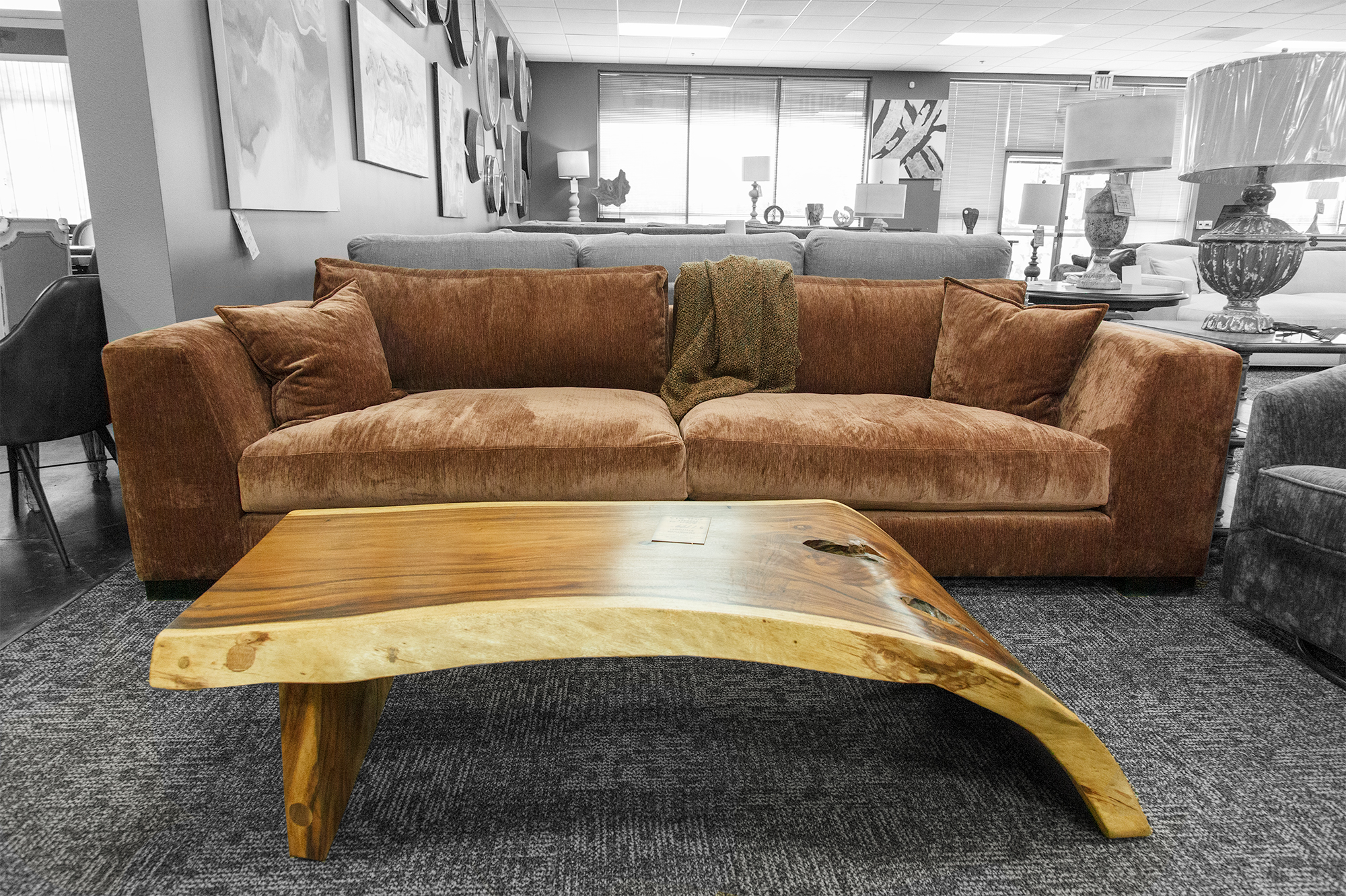 A plush brown sofa paired with a curved live-edge coffee table in a showroom with layered neutral tones.