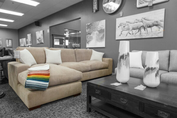 Beige sectional sofa with rainbow fabric swatches draped on the chaise lounge, displayed in a furniture showroom with neutral décor.