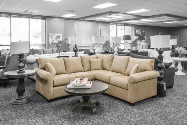 Soft beige sectional with classic lines and a round black coffee table, displayed in a sunlit showroom with coordinated decor.