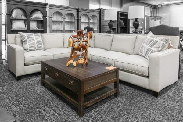 Neutral cream-colored sectional sofa paired with a dark wood coffee table featuring carved details and sculptural decor on top.
