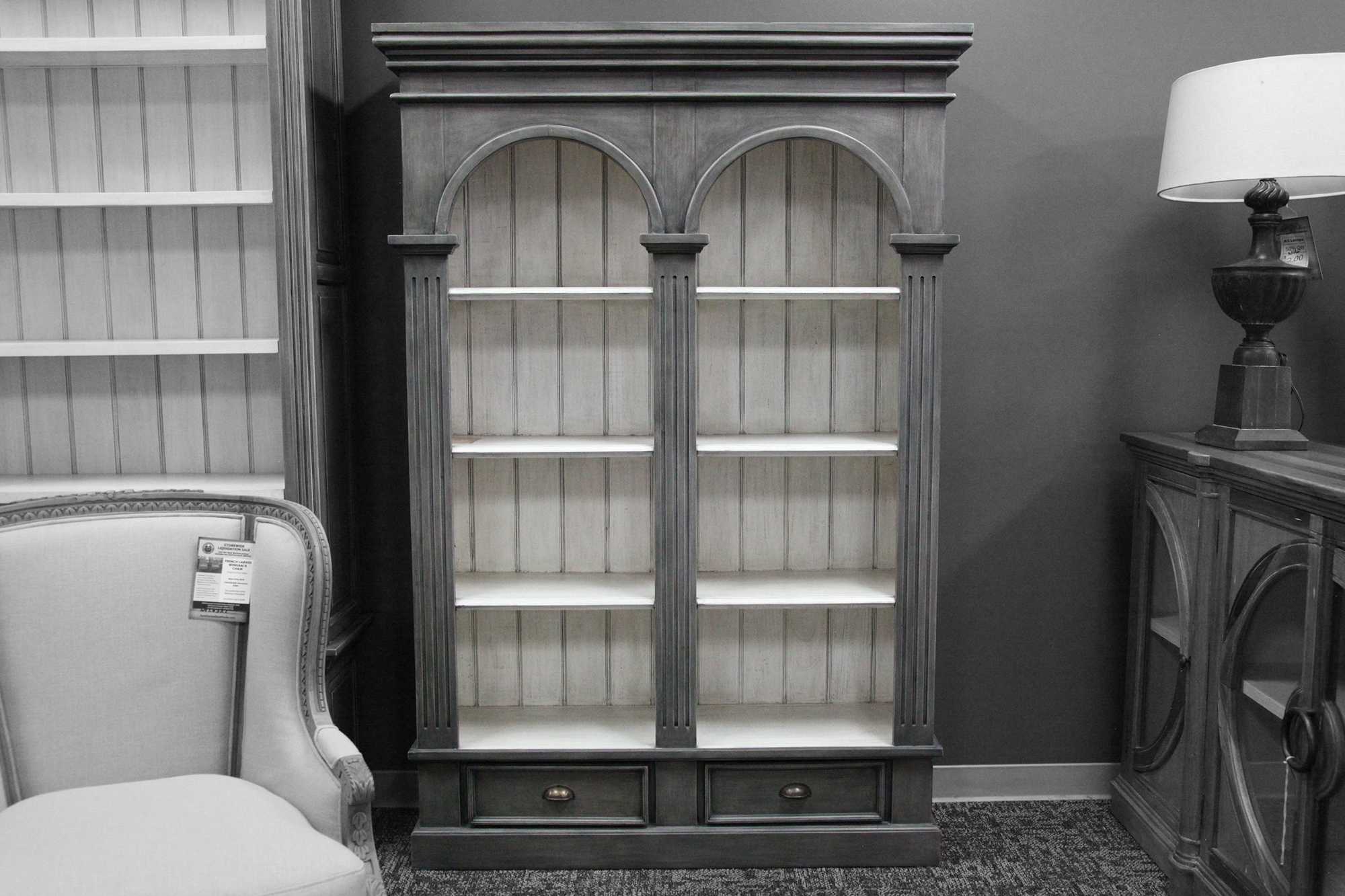 A tall grey double arch bookcase with 6 shelves, 3 on each side. There are also two storage drawers on the bottom.