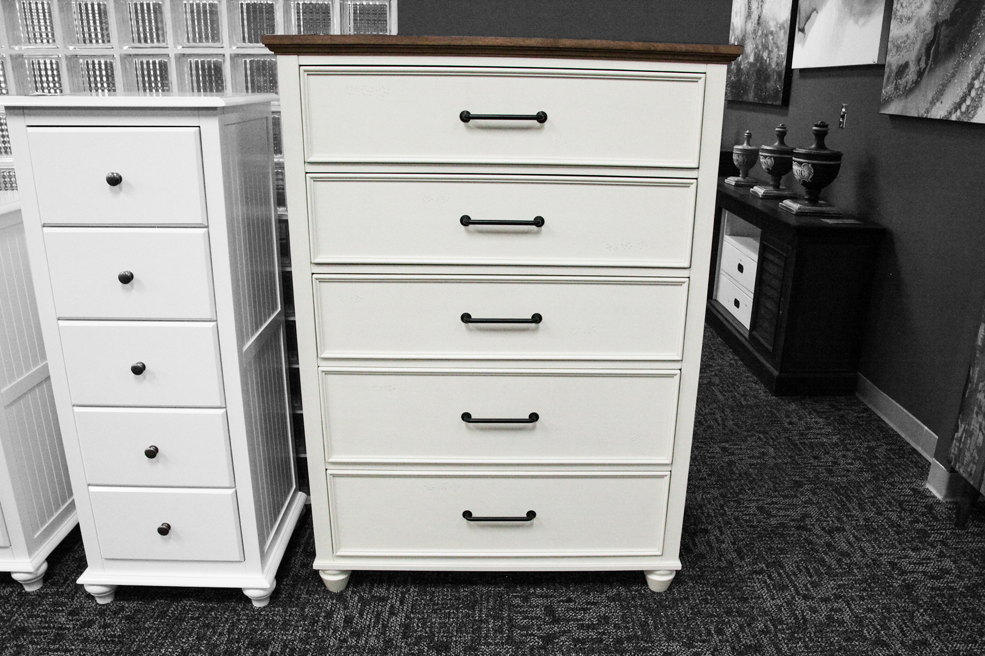 Tall, solid wood classic cream five-drawer chest, with a warm wood top. The chest is in the showroom next to another narrow five-drawer chest.